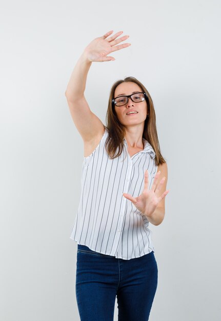 Giovane donna in t-shirt, jeans che mostrano i palmi sollevati e che sembrano divertenti, vista frontale.