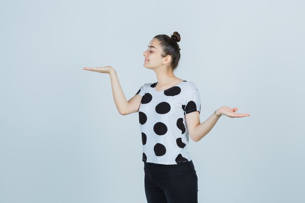 Giovane donna in t-shirt, jeans che mostrano il gesto delle scale mentre distoglie lo sguardo e sembra felice, vista frontale.