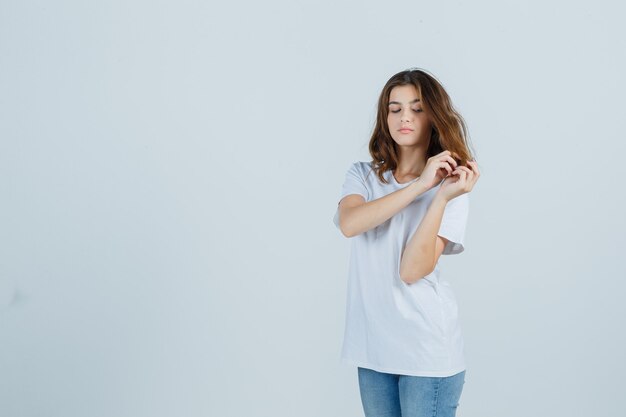 Giovane donna in t-shirt, jeans tenendo una ciocca di capelli e guardando pensieroso, vista frontale.