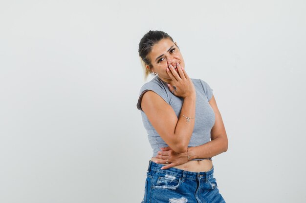 Giovane donna in t-shirt, pantaloncini tenendo la mano sulla bocca