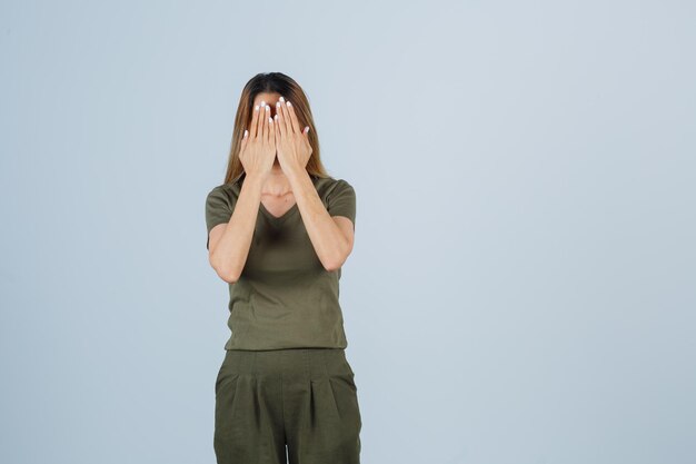 Giovane donna in t-shirt, pantaloni che si tengono per mano sul viso e sembra spaventata, vista frontale.