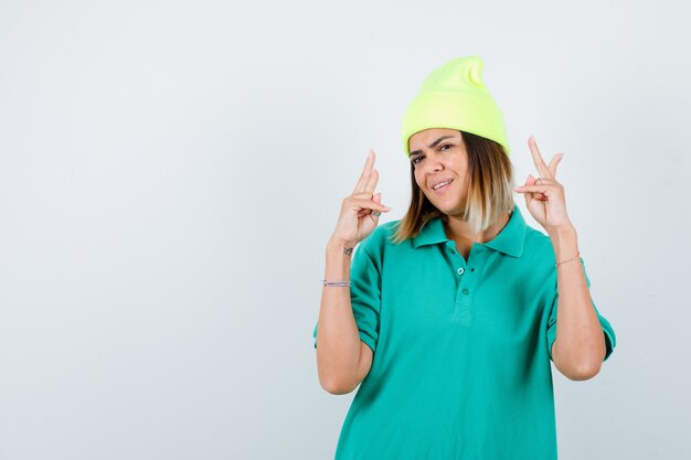 Giovane donna in t-shirt polo, berretto che mostra gesto di vittoria e sembra allegro, vista frontale.