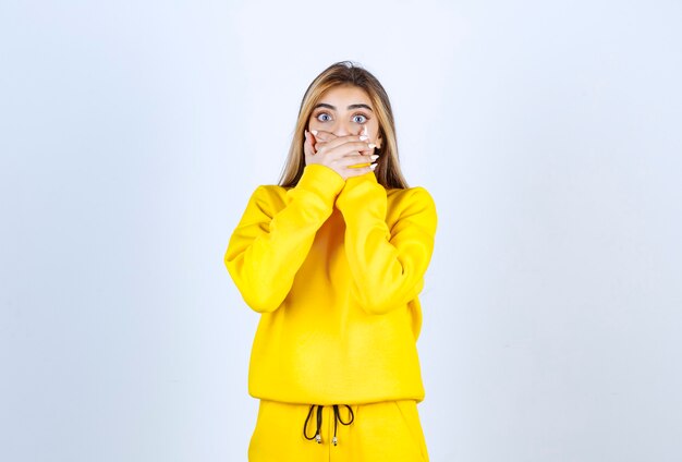 Giovane donna in tuta gialla che si copre la bocca sul muro bianco