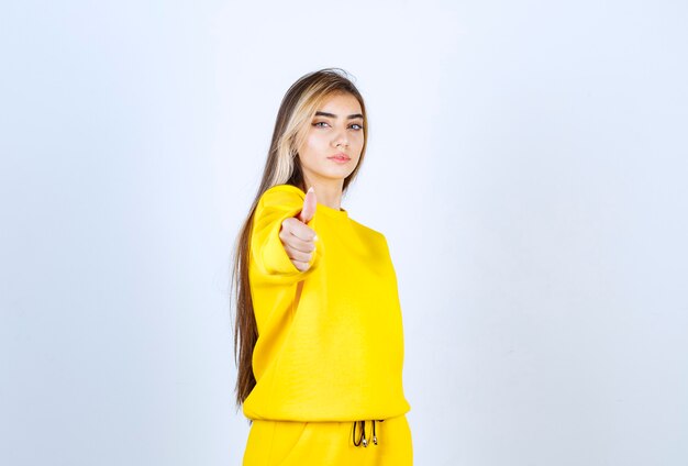Giovane donna in tuta gialla in posa per la telecamera su muro bianco