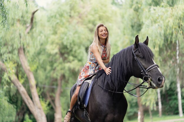 Giovane donna in un abito colorato luminoso a cavallo nero