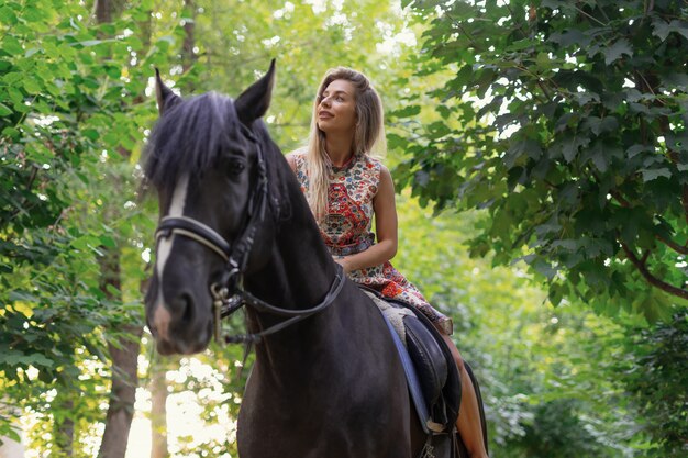 Giovane donna in un abito colorato luminoso a cavallo nero