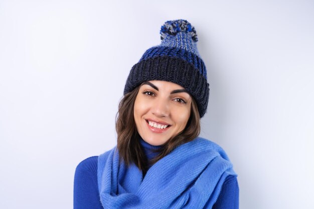 Giovane donna in un cappello a collo alto da golf blu e sciarpa su sfondo bianco allegro di buon umore