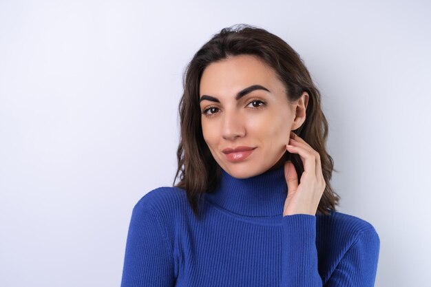 Giovane donna in un dolcevita da golf blu su sfondo bianco guardando la telecamera con un sorriso fiducioso