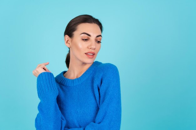 Giovane donna in un maglione lavorato a maglia blu e trucco naturale diurno su uno sfondo turchese, labbra carnose con rossetto opaco nudo, guarda in basso di lato