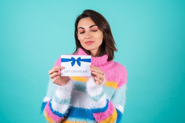 Giovane donna in un maglione multicolore luminoso su blu che tiene un buono regalo