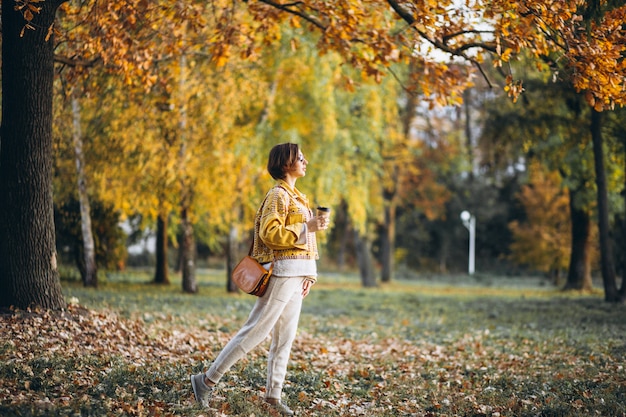 Giovane donna in un parco di autunno che beve caffè