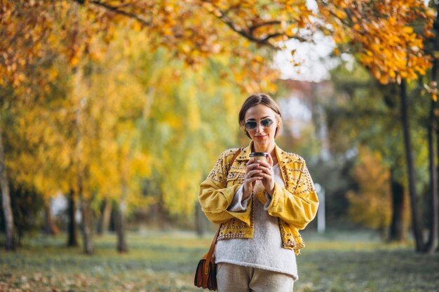 Giovane donna in un parco di autunno che beve caffè