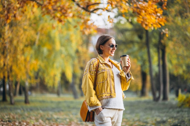 Giovane donna in un parco di autunno che beve caffè