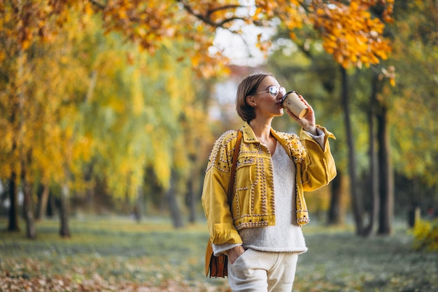 Giovane donna in un parco di autunno che beve caffè