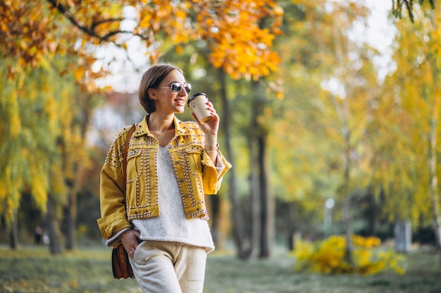 Giovane donna in un parco di autunno che beve caffè