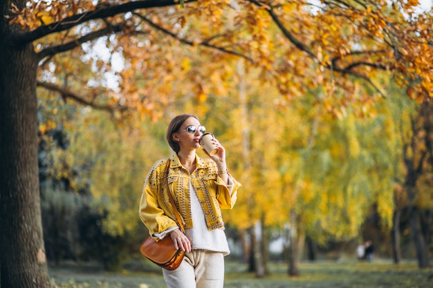 Giovane donna in un parco di autunno che beve caffè