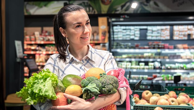 Giovane donna in un supermercato con frutta e verdura che acquistano generi alimentari