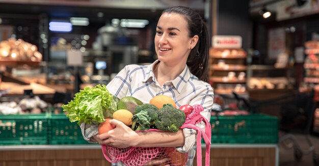 Giovane donna in un supermercato con frutta e verdura che acquistano generi alimentari