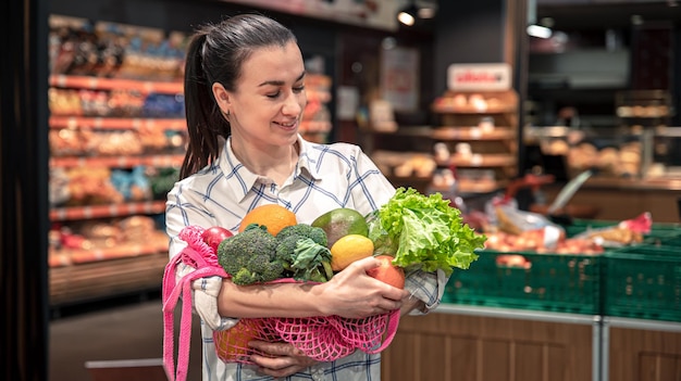 Giovane donna in un supermercato con frutta e verdura che acquistano generi alimentari