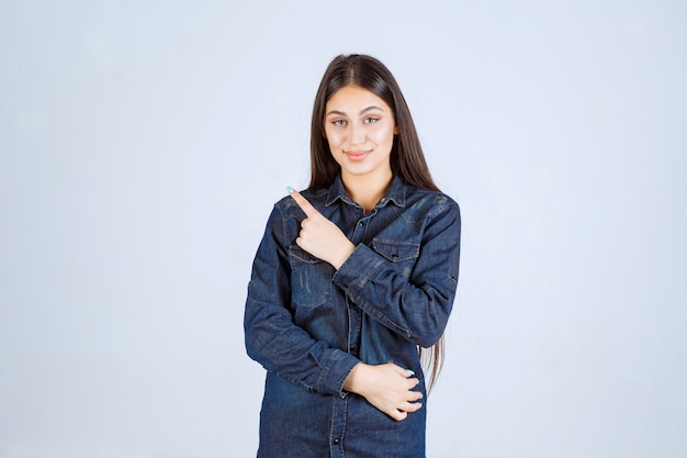 Giovane donna in una camicia di jeans che punta a sinistra con le emozioni del viso