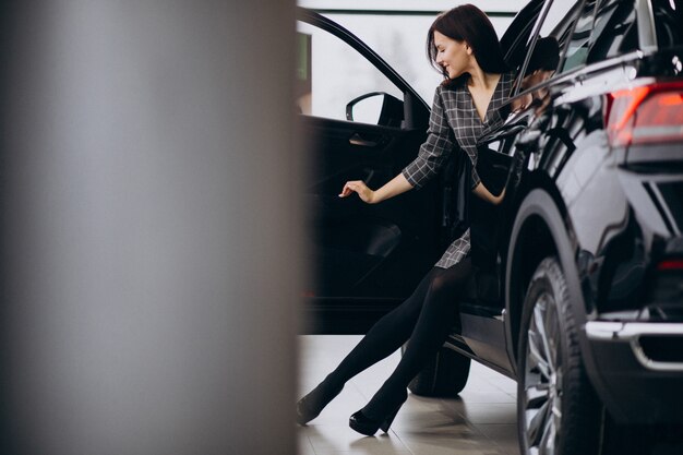 Giovane donna in una sala d'esposizione dell'automobile che sceglie un'automobile