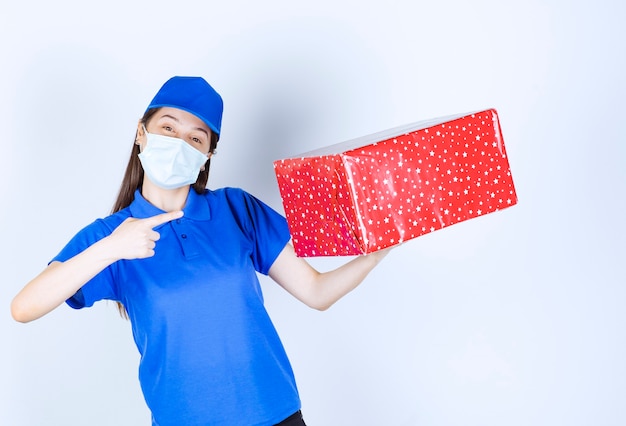 Giovane donna in uniforme e maschera medica che punta al regalo di Natale.