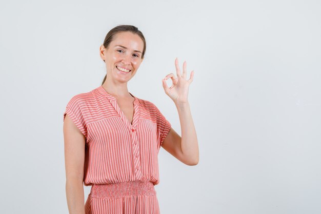 Giovane donna in vestito a strisce che mostra gesto giusto e che sembra allegra, vista frontale.