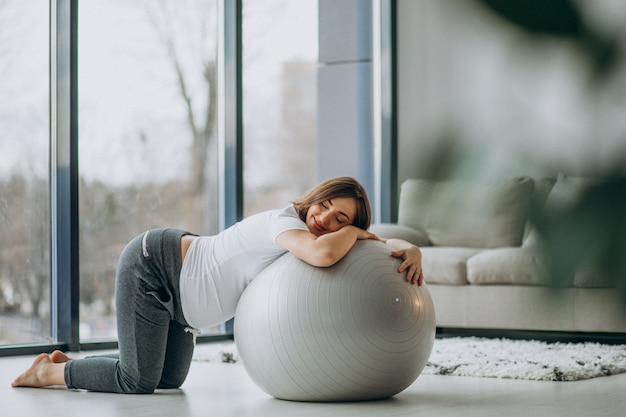 Giovane donna incinta che esercita yoga con la palla di misura a casa