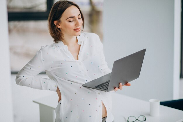 Giovane donna incinta che lavora al computer fuori dall'ufficio