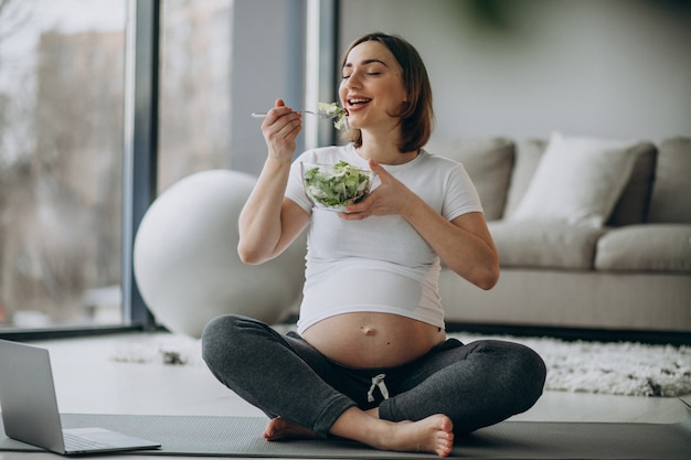 Giovane donna incinta che mangia insalata a casa