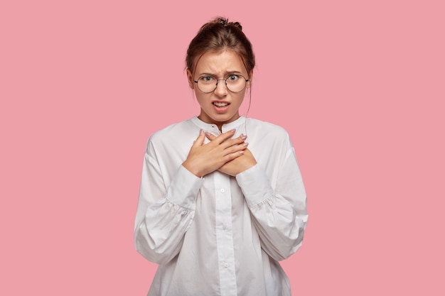 Giovane donna infastidita scontenta con gli occhiali in posa contro il muro rosa