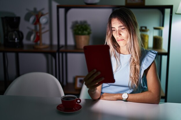 Giovane donna ispanica che utilizza il touchpad seduta sul tavolo di notte depressa e si preoccupa per l'angoscia piangendo espressione triste arrabbiata e impaurita