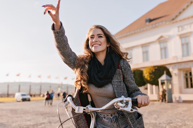 Giovane donna ispirata in sciarpa nera che guida sulla bicicletta intorno alla città europea