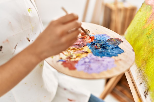 Giovane donna latina che mescola colore sulla tavolozza in studio d'arte