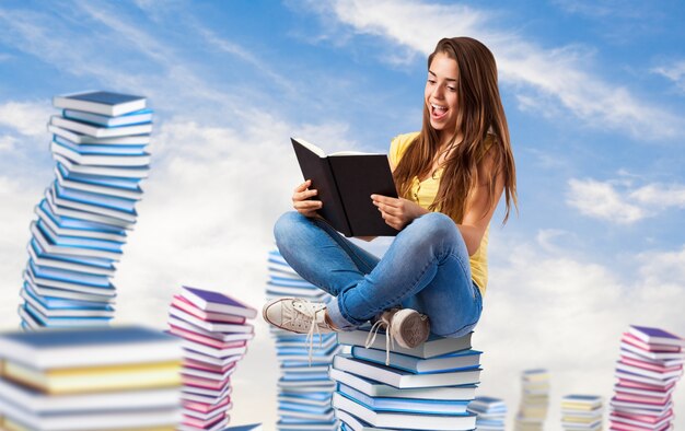 giovane donna leggendo un libro seduto su una pila di libri sul cielo