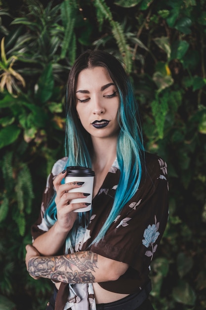 Giovane donna moderna con capelli tinti che tengono la tazza di caffè asportabile