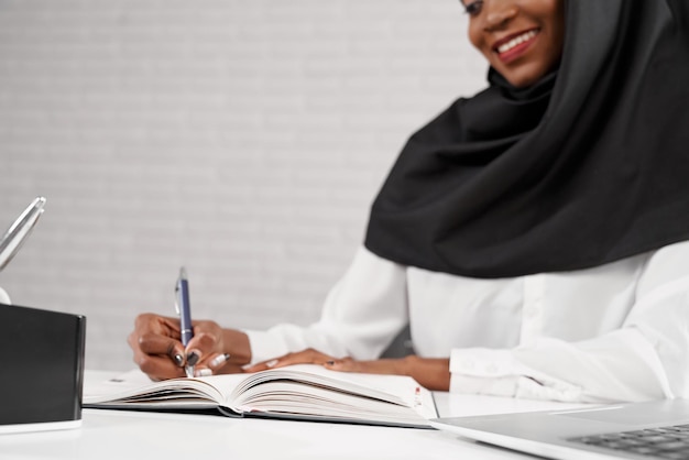 Giovane donna musulmana africana seduta sul posto di lavoro a scrivere