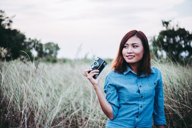 Giovane donna pantaloni a vita bassa che fa le foto con la macchina fotografica della pellicola dell&#39;annata al campo estivo. Le donne concetto di lifestyle.