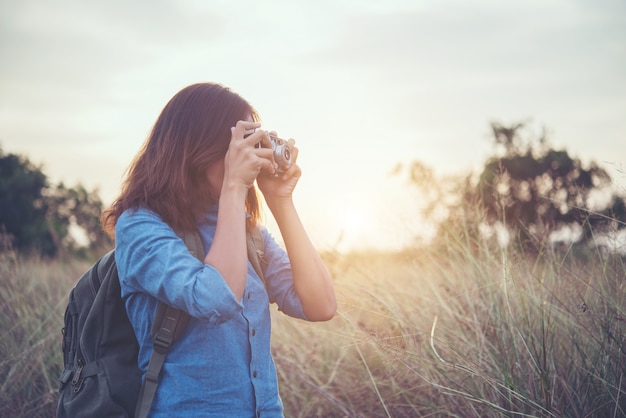 Giovane donna pantaloni a vita bassa che fa le foto con la macchina fotografica della pellicola dell&#39;annata al campo estivo. Le donne concetto di lifestyle.