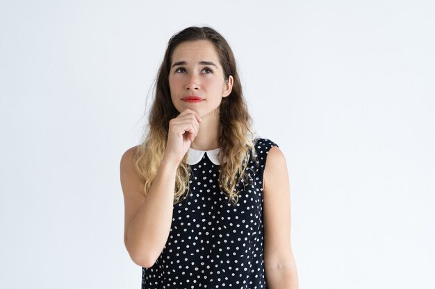 Giovane donna pensosa che tocca mento e alzando lo sguardo