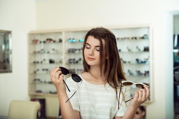 Giovane donna per lo shopping, in possesso di due paia di occhiali da sole alla moda