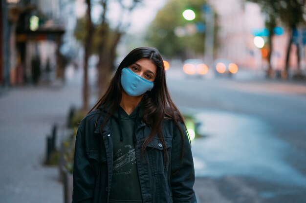 Giovane donna, persona in maschera protettiva sterile medica in piedi in strada vuota, guardando la fotocamera.