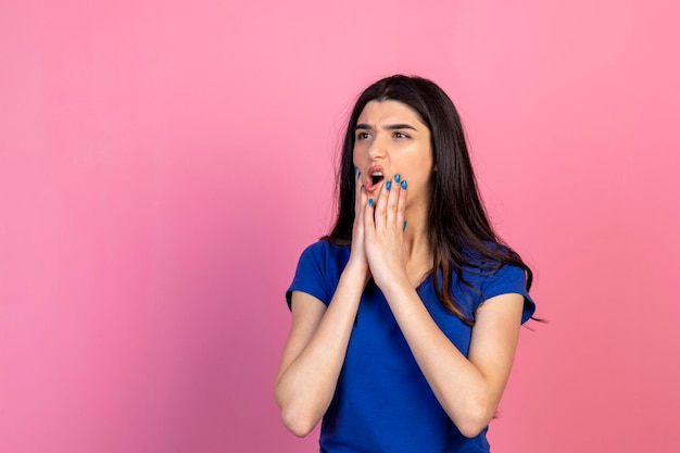 Giovane donna premurosa che si mette le mani sul viso e pensa su sfondo rosa Foto di alta qualità