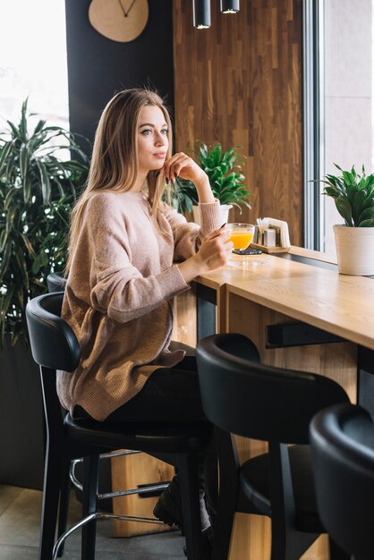 Giovane donna premurosa elegante che tiene tazza della bevanda al contatore della barra in caffè