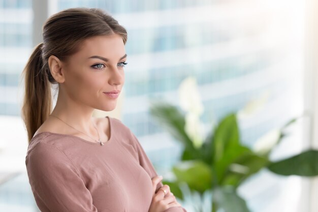 Giovane donna premurosa pensierosa che guarda attraverso la finestra, armi attraversate, all&#39;interno