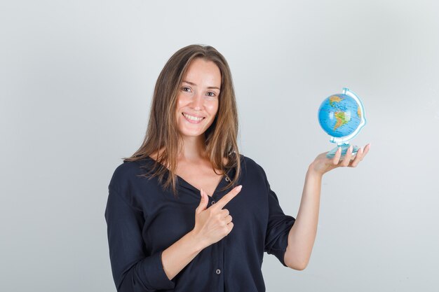 Giovane donna puntare il dito al globo in camicia nera e guardando allegro