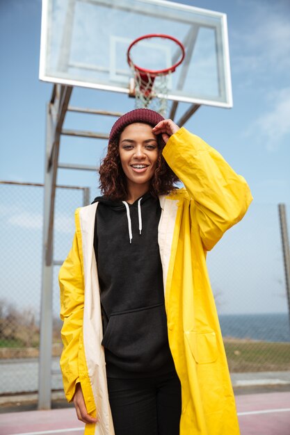 Giovane donna riccia africana felice che porta cappotto giallo