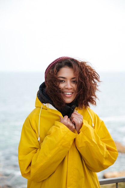 Giovane donna riccia africana felice che porta cappotto giallo