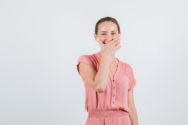 Giovane donna ridendo e tenendo la mano sulla bocca in abito a righe, vista frontale.