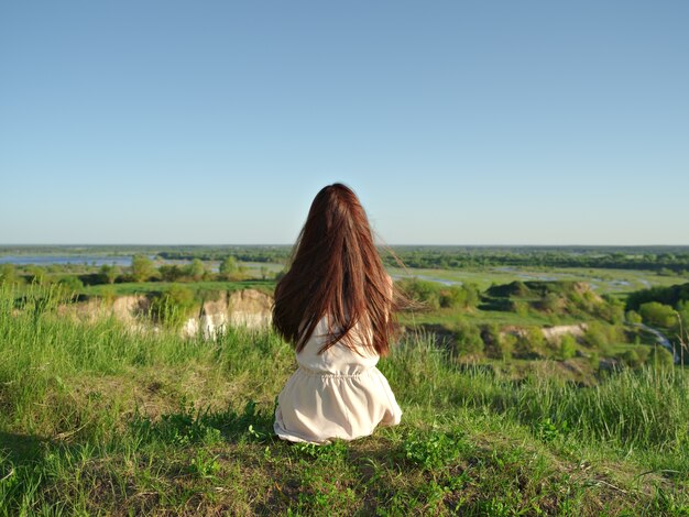 Giovane donna rilassata che guarda nella vista. Ubicazione pacifica della ragazza da una scogliera che gode del paesaggio. - all'aperto